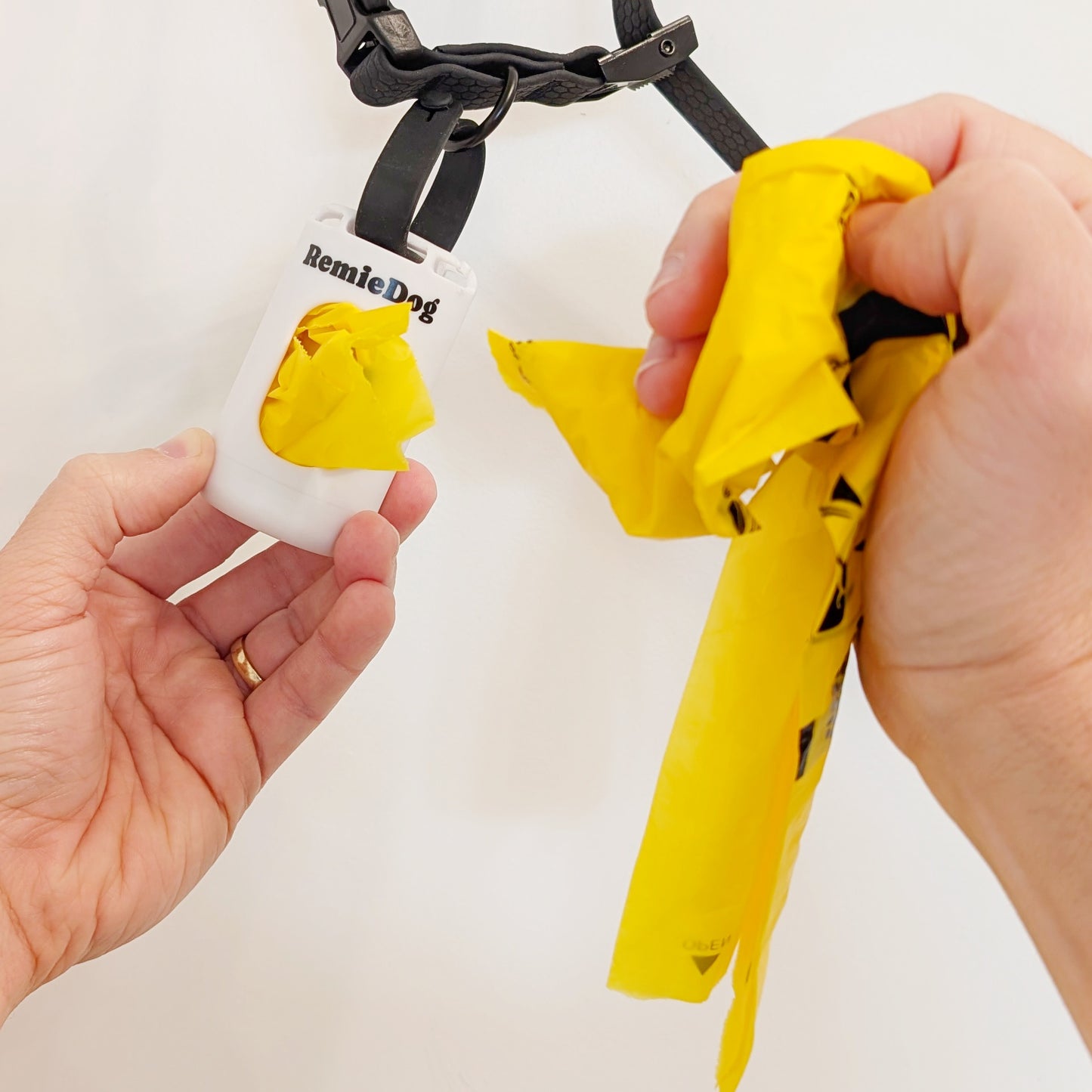 Person pulling a compostable yellow dog poop bag out of a remiedog poop bag dispenser