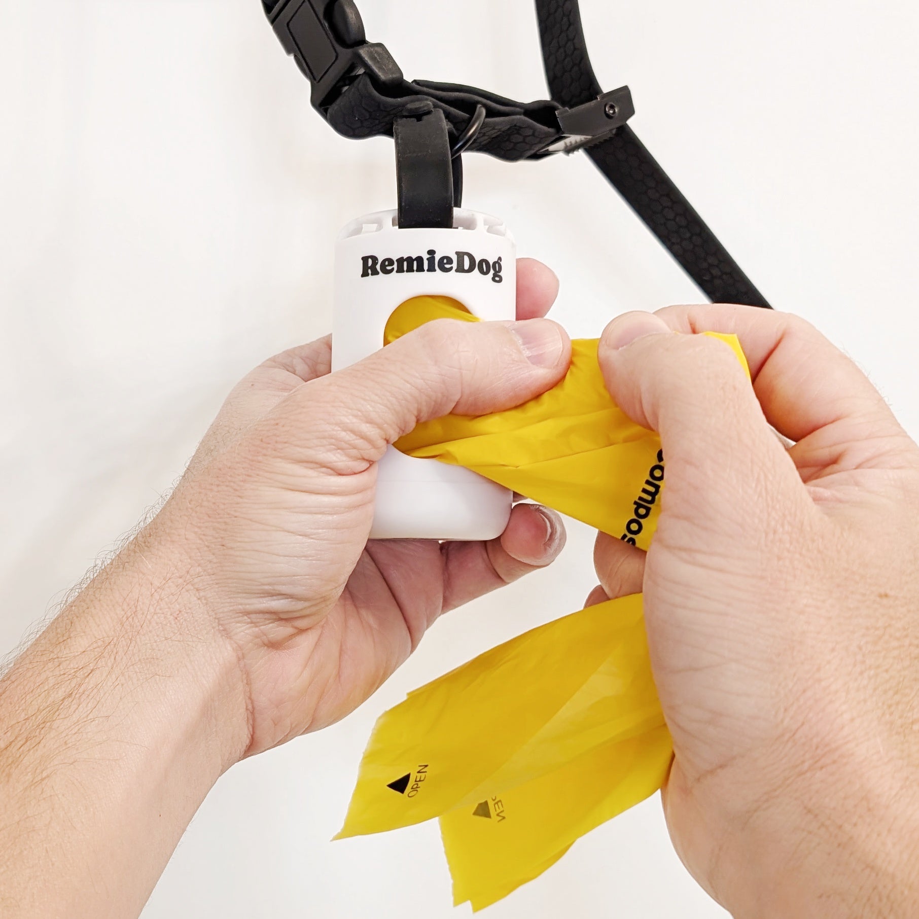 Person using a yellow dog waste bag dispenser with 'RemieDog' branding on a white background