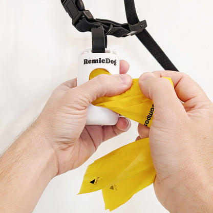 Person using a yellow dog waste bag dispenser with 'RemieDog' branding on a white background