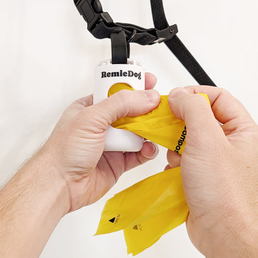 Person using a yellow dog waste bag dispenser with 'RemieDog' branding on a white background